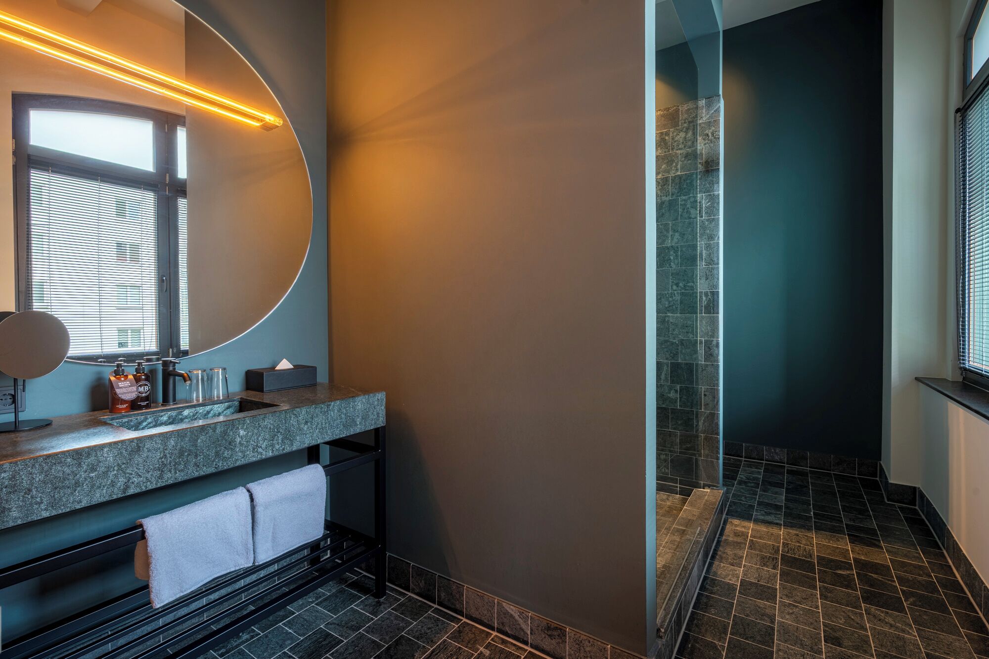 Ein modernes Badezimmer mit einem gewölbten Spiegel, einem Waschbecken mit Marmorplatte und einer Duschkabine aus Glas.