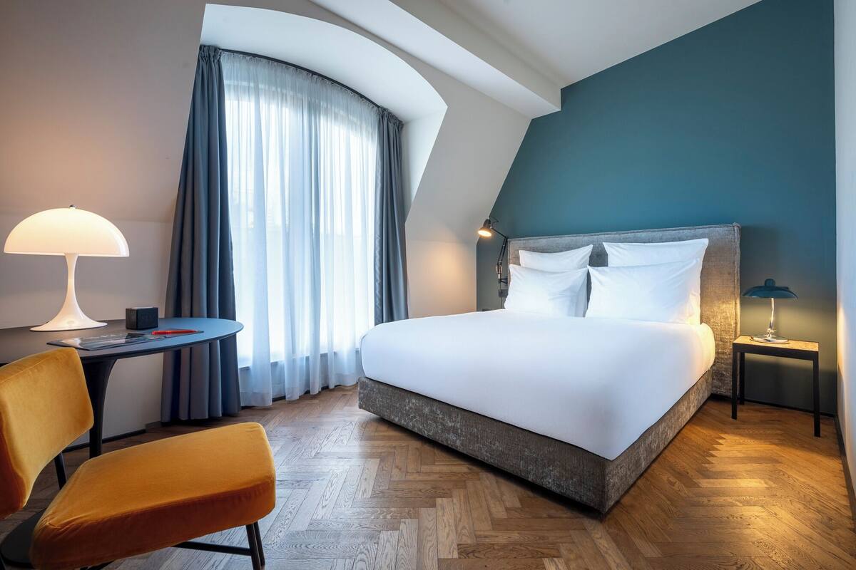 A hotel room with a bed, a desk, a chair, and a window with curtains.