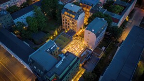 Oversigtsbillede af et moderne byområde med en blanding af boliger og erhvervsbygninger, hvor et markant byggeri med glasloft og flere etager samt en tagterrasse fremhæves.