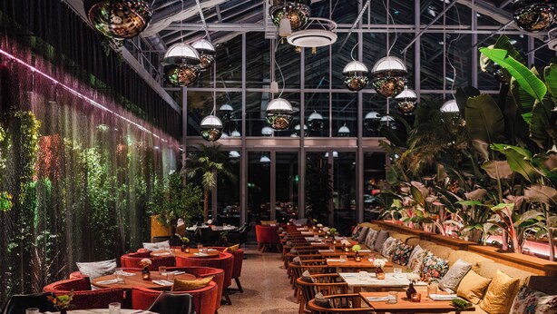 En restaurant med runde borde og røde stole, et hvælvet loft med hængende lys og en grøn væg.