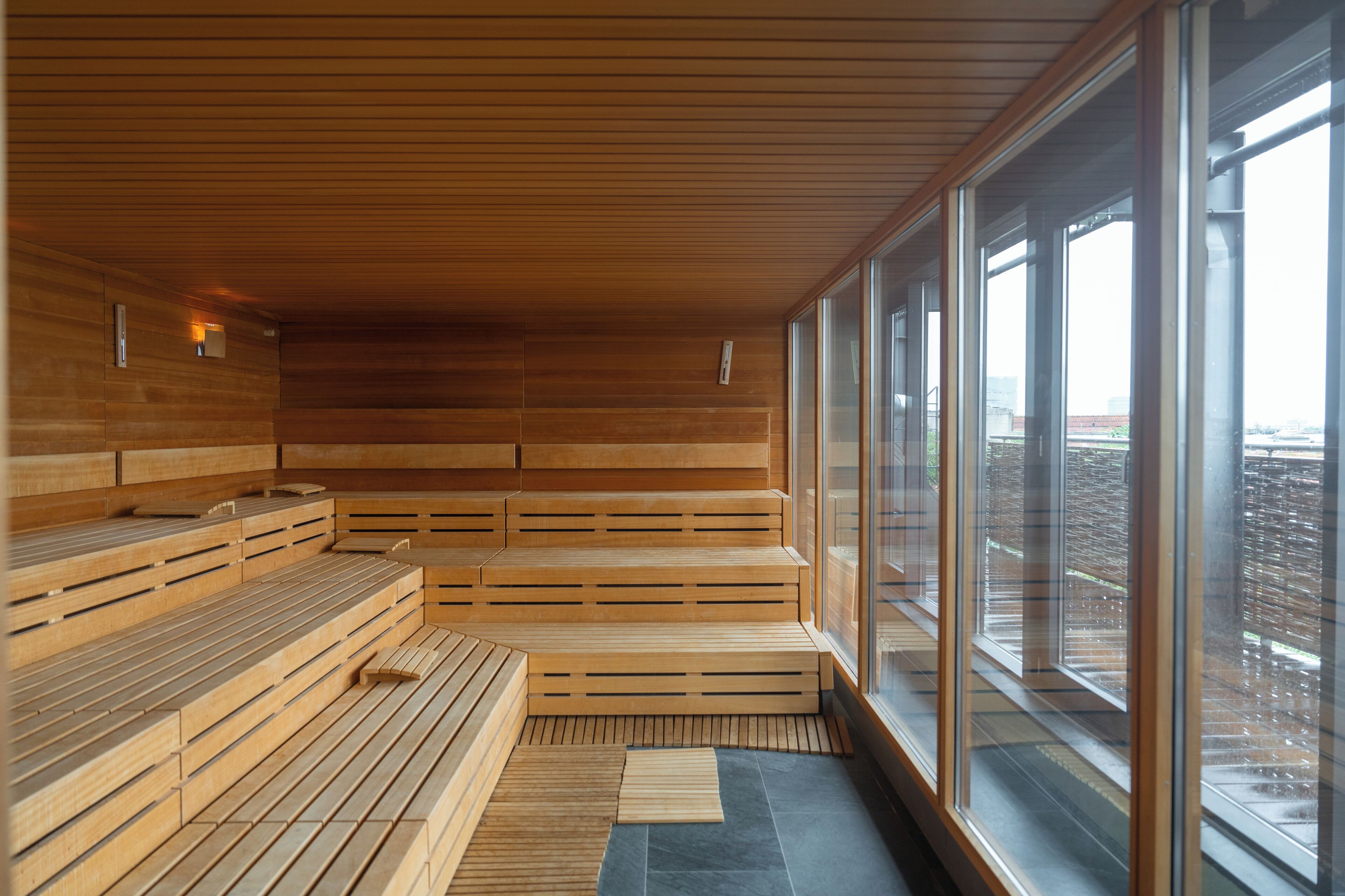 Una sauna moderna con bancos de madera y grandes ventanales con vistas a la ciudad.