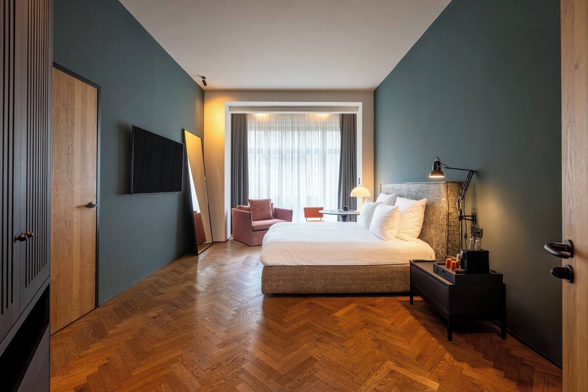 A modern hotel room with a large bed, a flat-screen TV, a desk with a lamp, and a chair.