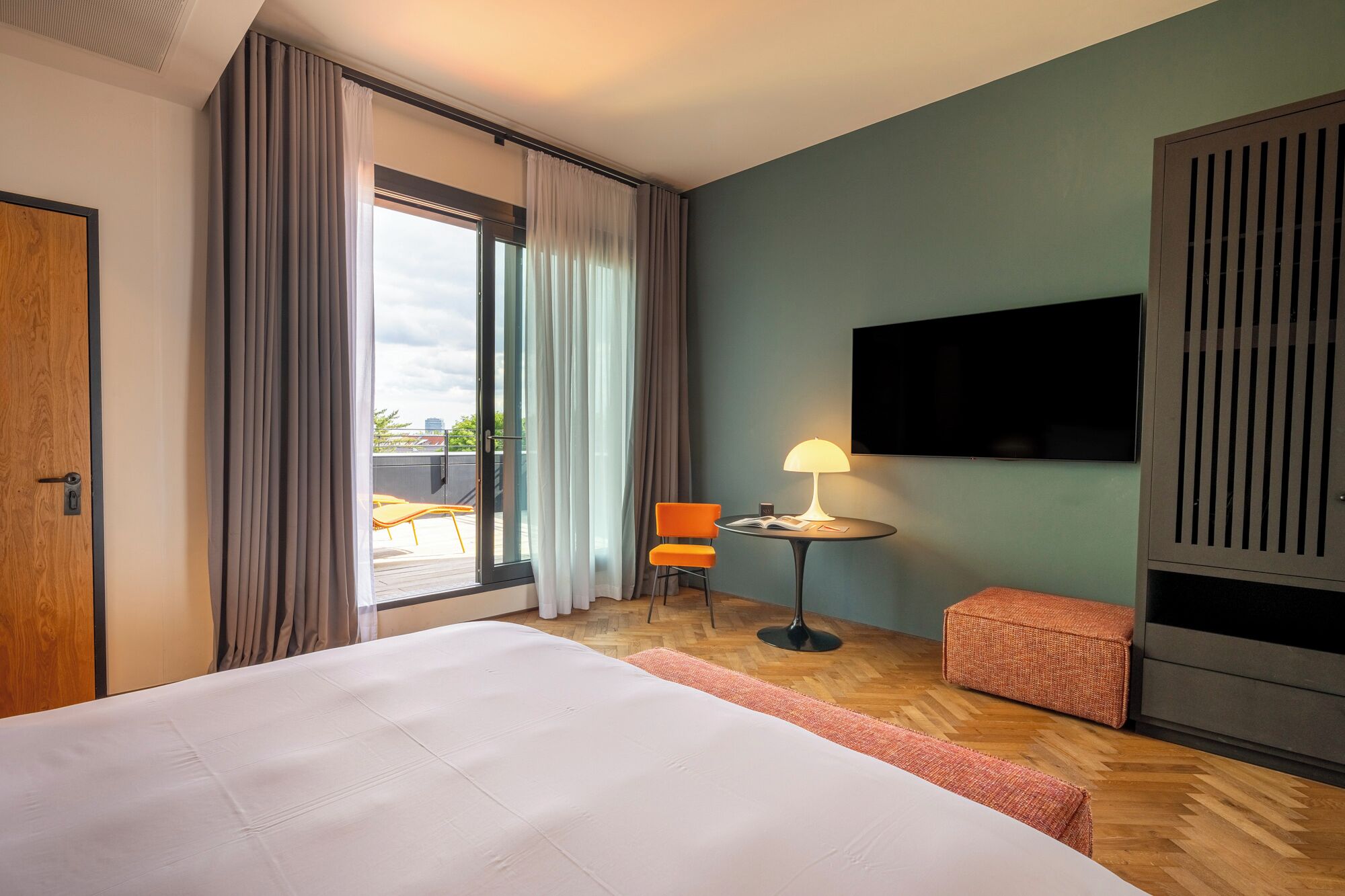 Una camera d'albergo con un letto, un tavolino con una lampada, una TV e vista sull'esterno.