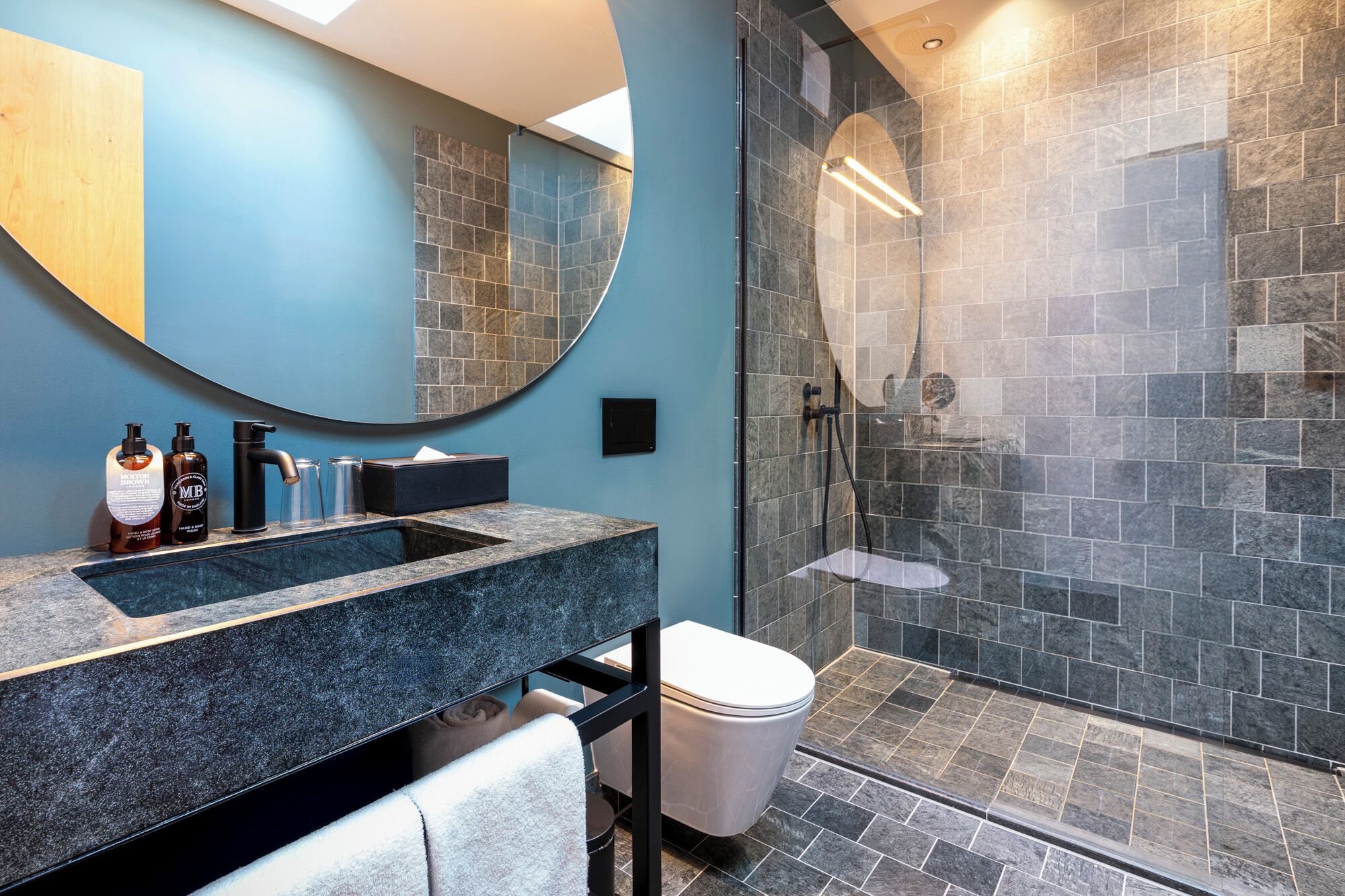 A modern bathroom with a granite sink, a large mirror, a glass-enclosed shower, and a toilet.
