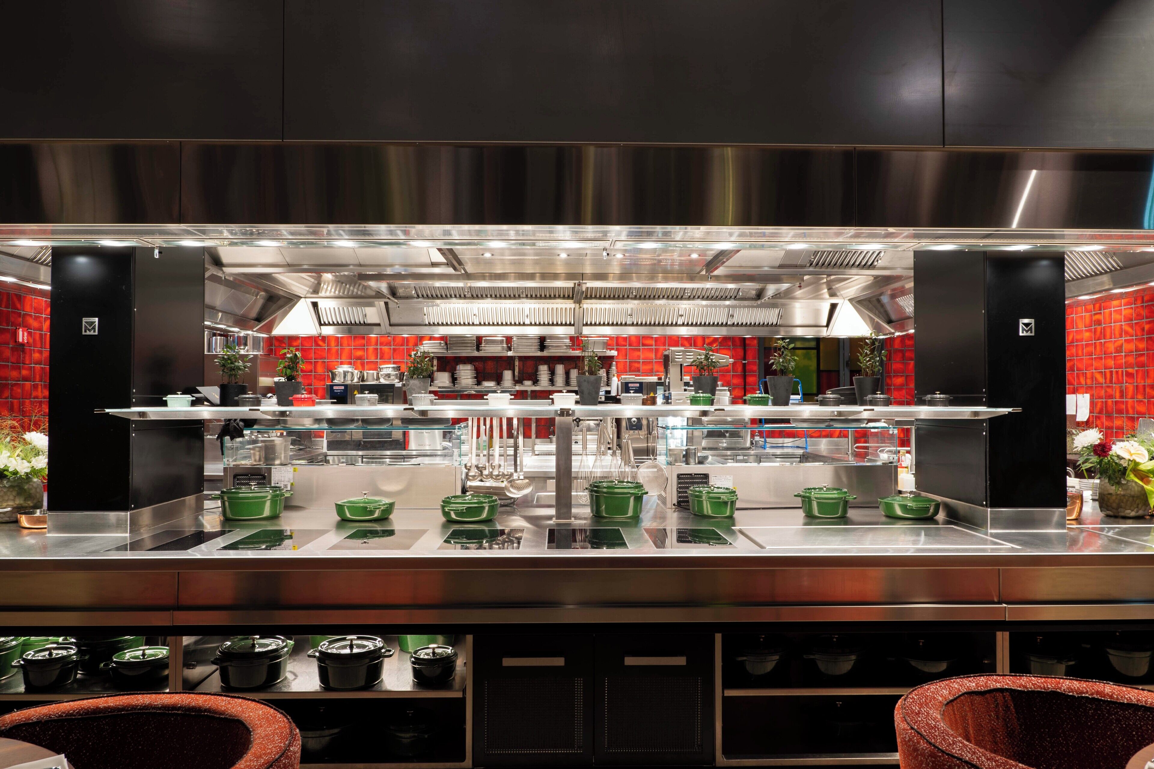Una cocina moderna con electrodomésticos de acero inoxidable, paredes de azulejos rojos y utensilios de cocina verdes sobre la encimera.