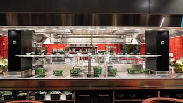 Una cocina moderna con electrodomésticos de acero inoxidable, paredes de azulejos rojos y utensilios de cocina verdes sobre la encimera.