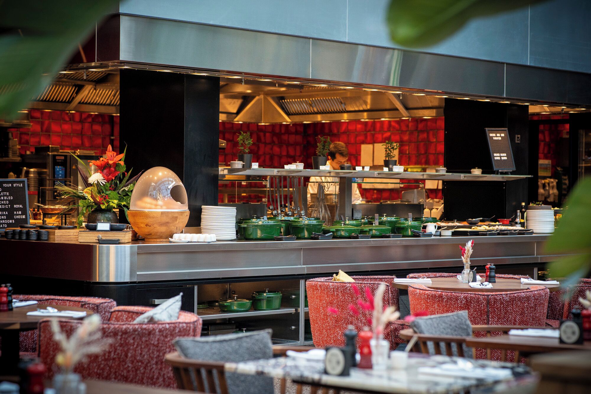 Een restaurant met een moderne keuken, rode bekleden stoelen en diverse gerechten gepresenteerd op de toonbank.
