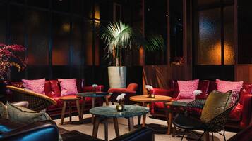 A dimly lit lounge area with leather sofas, round tables, and a large potted plant.