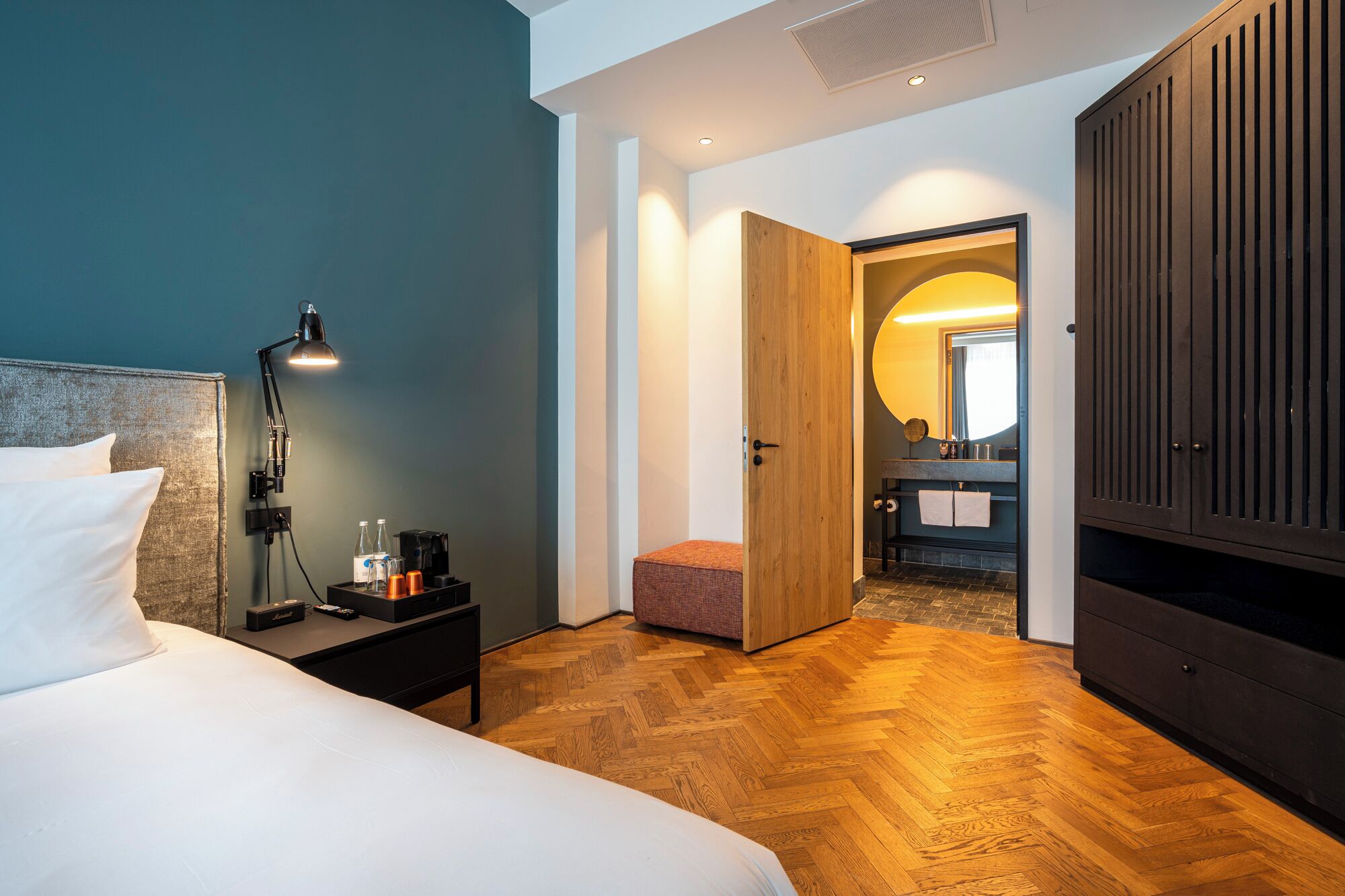 A hotel room with a bed, bedside table, lamp, and a wooden wardrobe.