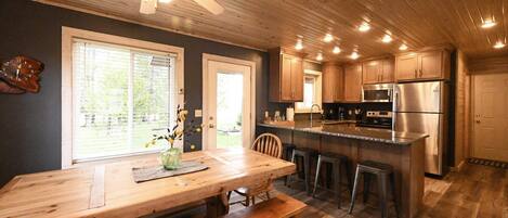 A kitchen with wooden cabinets, a stainless steel refrigerator, a wooden dining table with benches, and a ceiling fan.