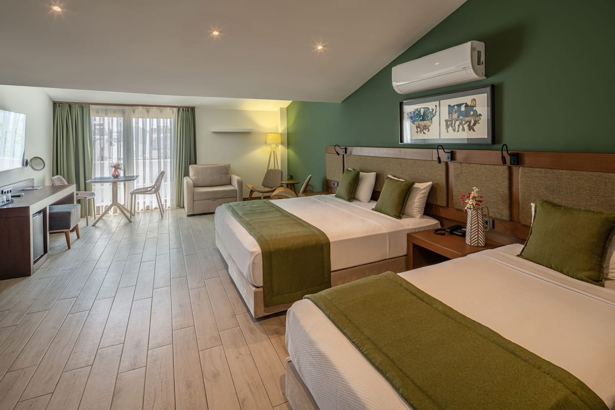 A hotel room with two beds, a desk, a chair, a lamp, and artwork on the wall.