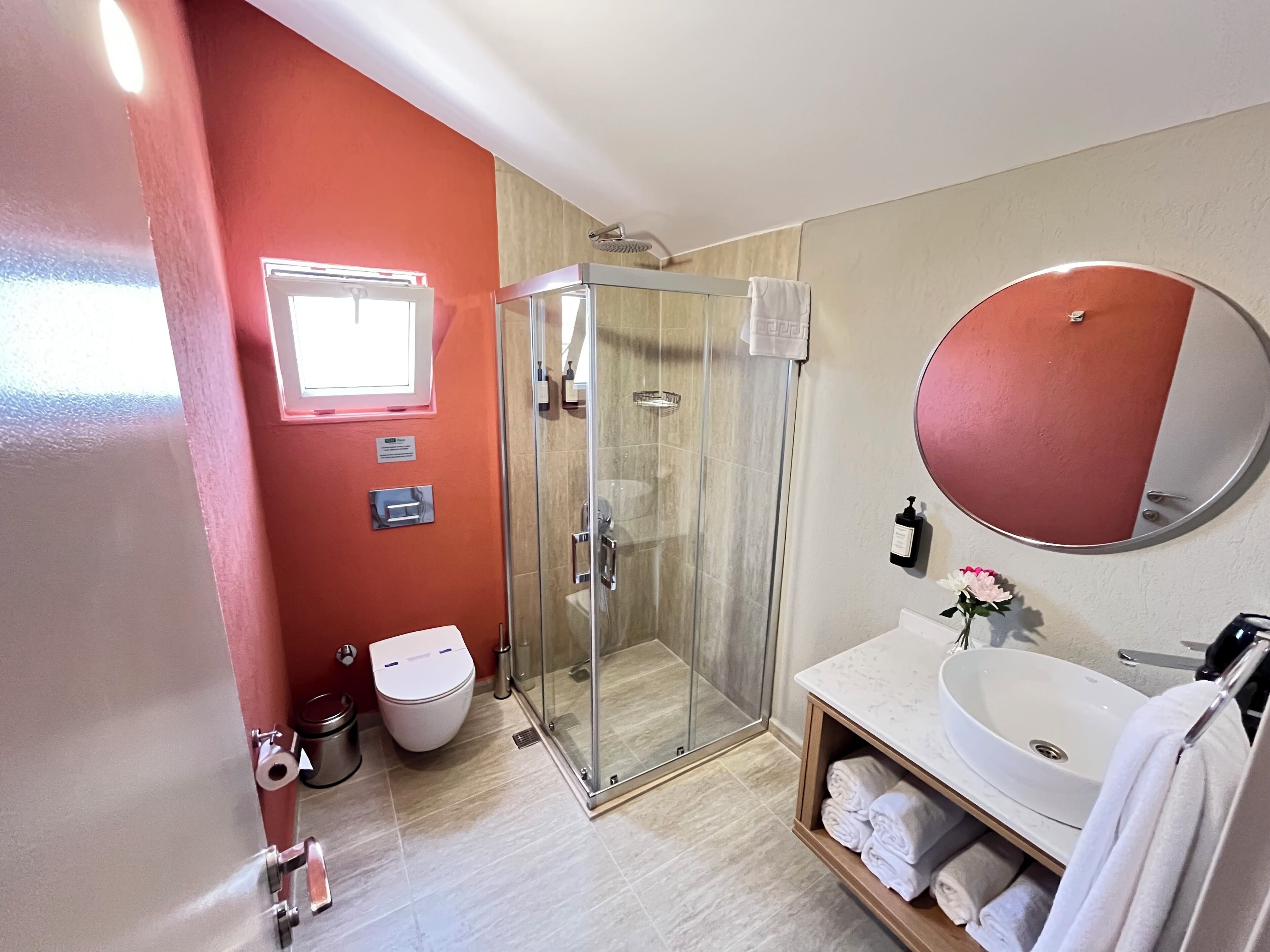 A bathroom with a glass-enclosed shower, a white toilet, a sink with a marble countertop, and a round mirror.