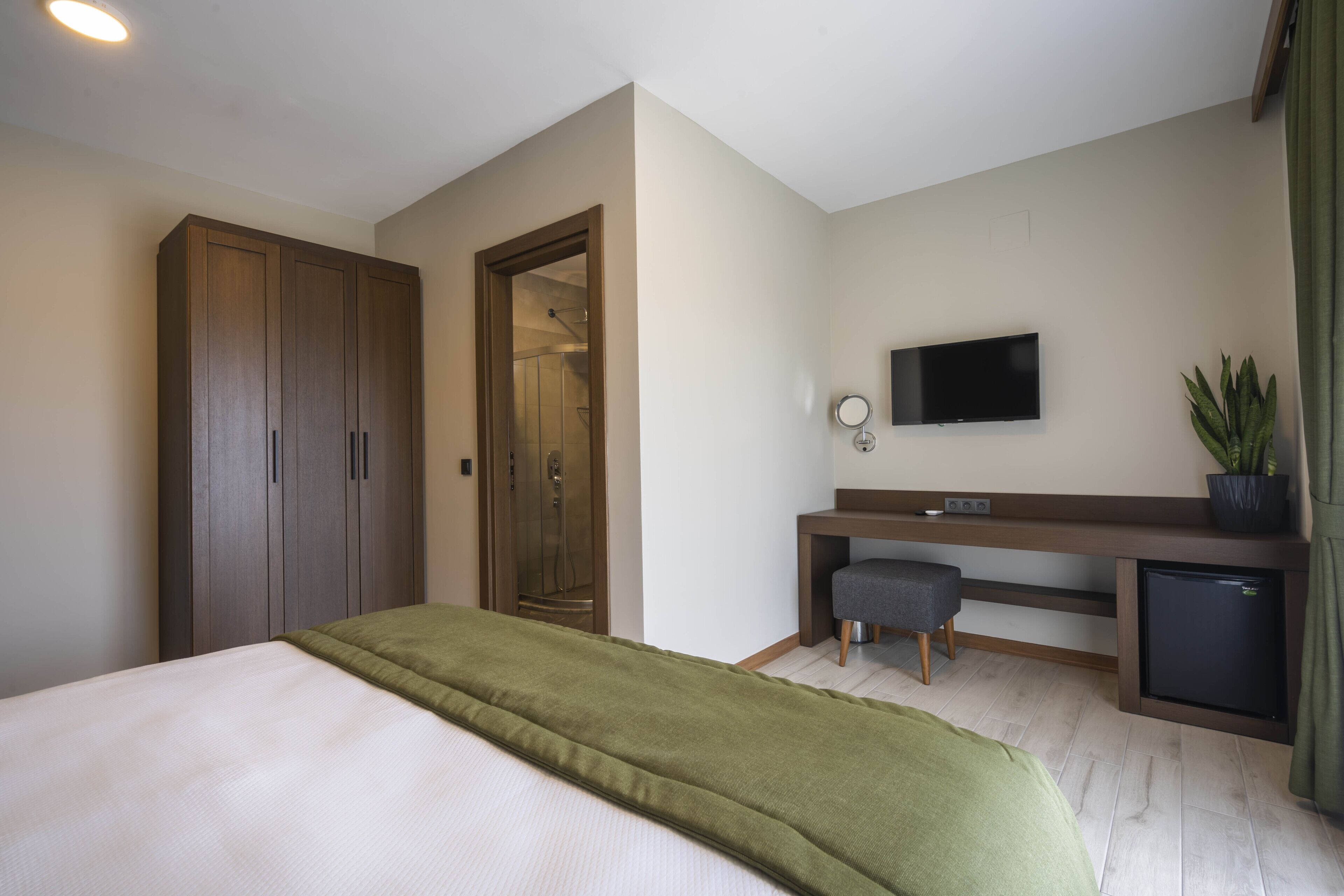Habitación de hotel con cama, escritorio con televisor, refrigerador pequeño y espejo.