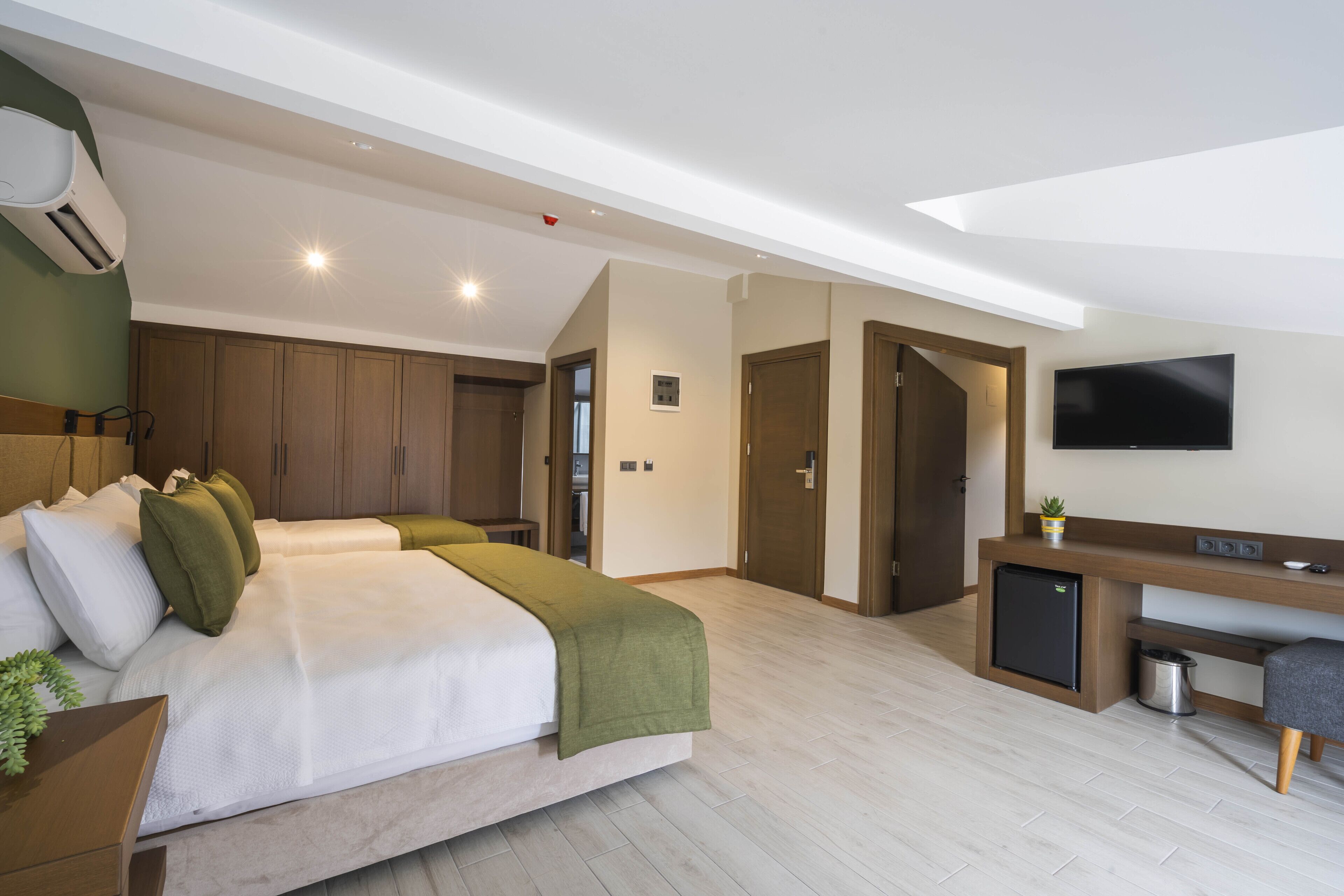Una habitación de hotel moderna con una cama grande, un escritorio, un televisor y un aire acondicionado.