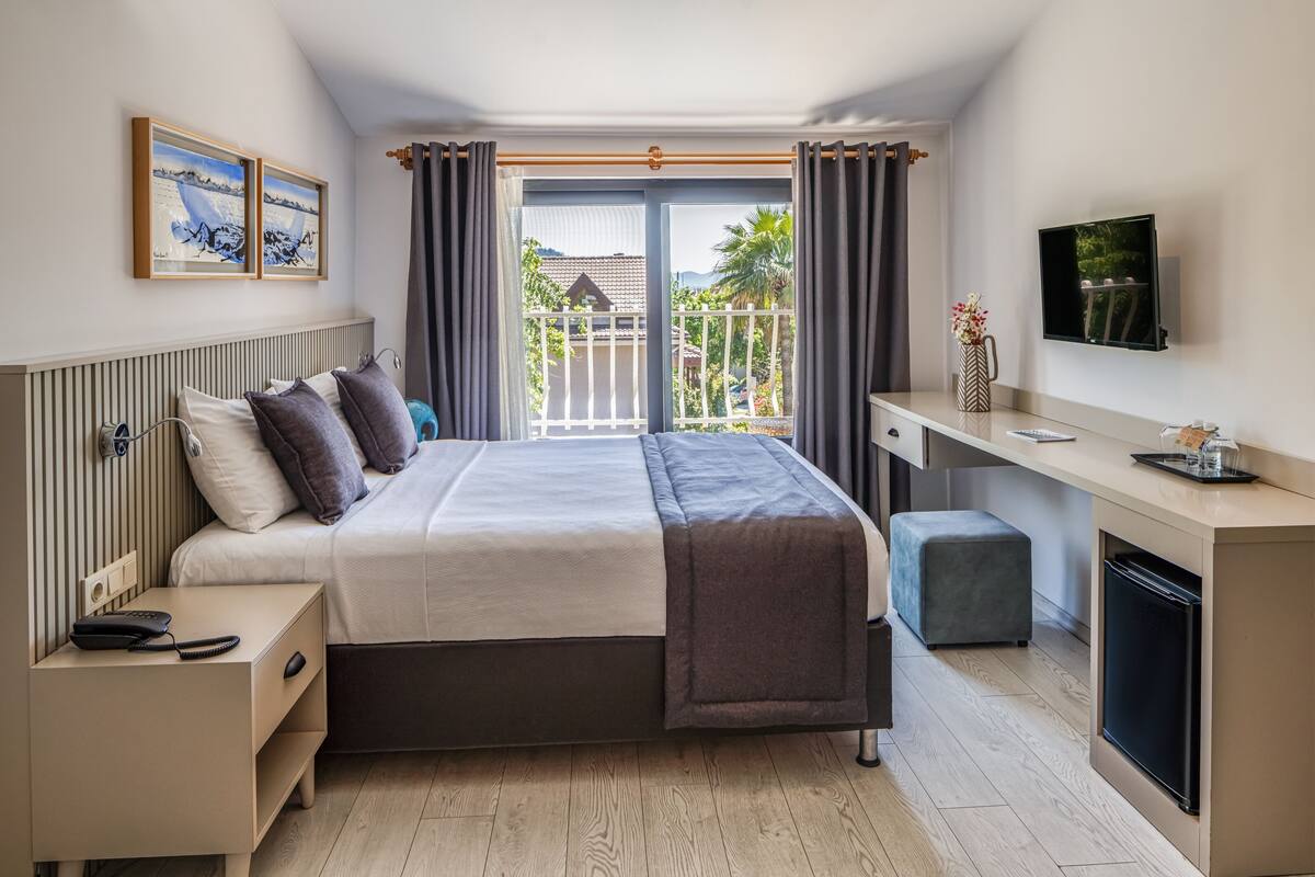 A modern hotel room with a bed, bedside table, desk, and a TV.