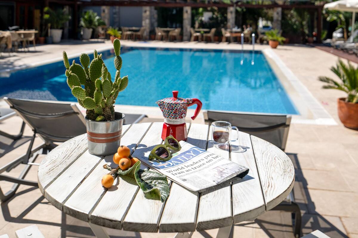 A poolside area with a table, chairs, a cactus, a pitcher, and a newspaper.
