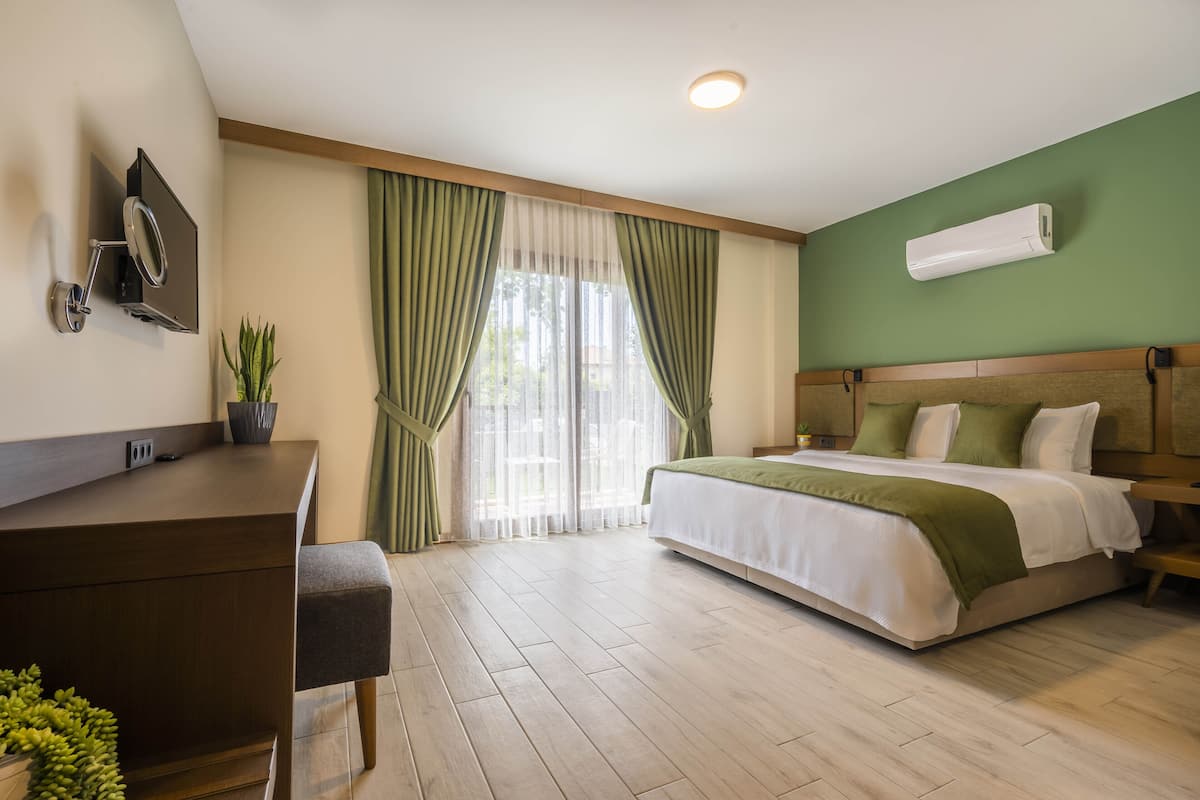 A hotel room with a bed, a desk, a chair, a TV mounted on the wall, and a window with curtains.