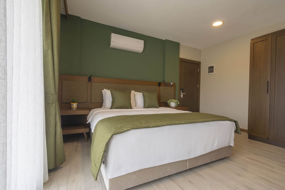 A hotel room with a large bed, a wooden headboard, a bedside table with a plant, and a green wall.