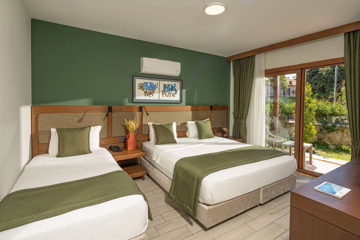 A hotel room with two beds, a desk, a chair, a window with curtains, and a framed picture on the wall.