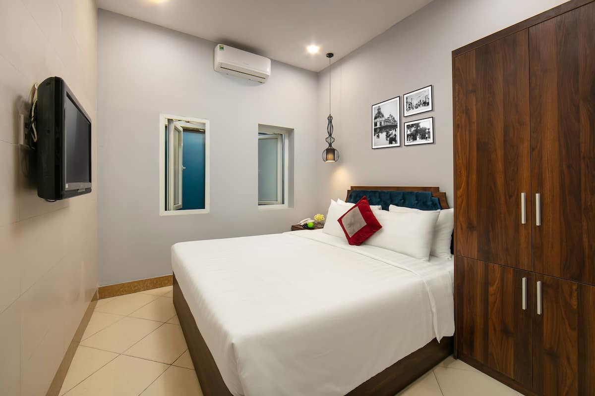 Une chambre à coucher comprenant un lit, une armoire, un téléviseur, un appareil de climatisation et deux fenêtres.