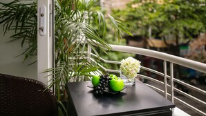 A balcony with a wicker chair, a small table with a green apple, grapes, and a vase of flowers. - Sonata Central Hotel & Spa (Hanoi)