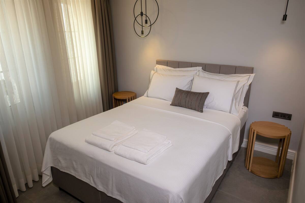 A neatly made bed with white linens and pillows, a bedside table, and a wall-mounted light fixture.