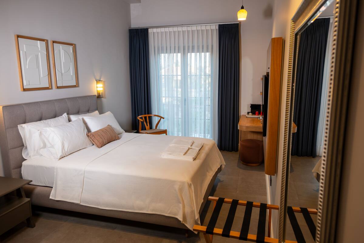 A neatly made bed with pillows and a folded towel, a bedside table, a chair, a lamp, and a mirror.