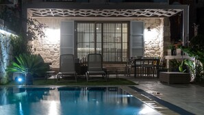 A poolside area with a stone wall, outdoor furniture, and a covered seating area. - Zena Hotel Alaçatı Adults Only (Cesme)
