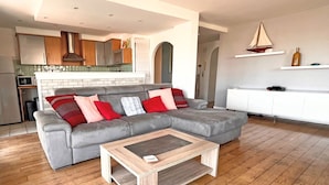 Een moderne woonkamer met een grijze modulaire bank, een houten salontafel en een keuken op de achtergrond.