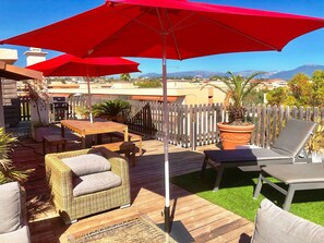 Una terraza de madera con mobiliario exterior, incluyendo sillas de mimbre y una mesa, bajo sombrillas rojas.