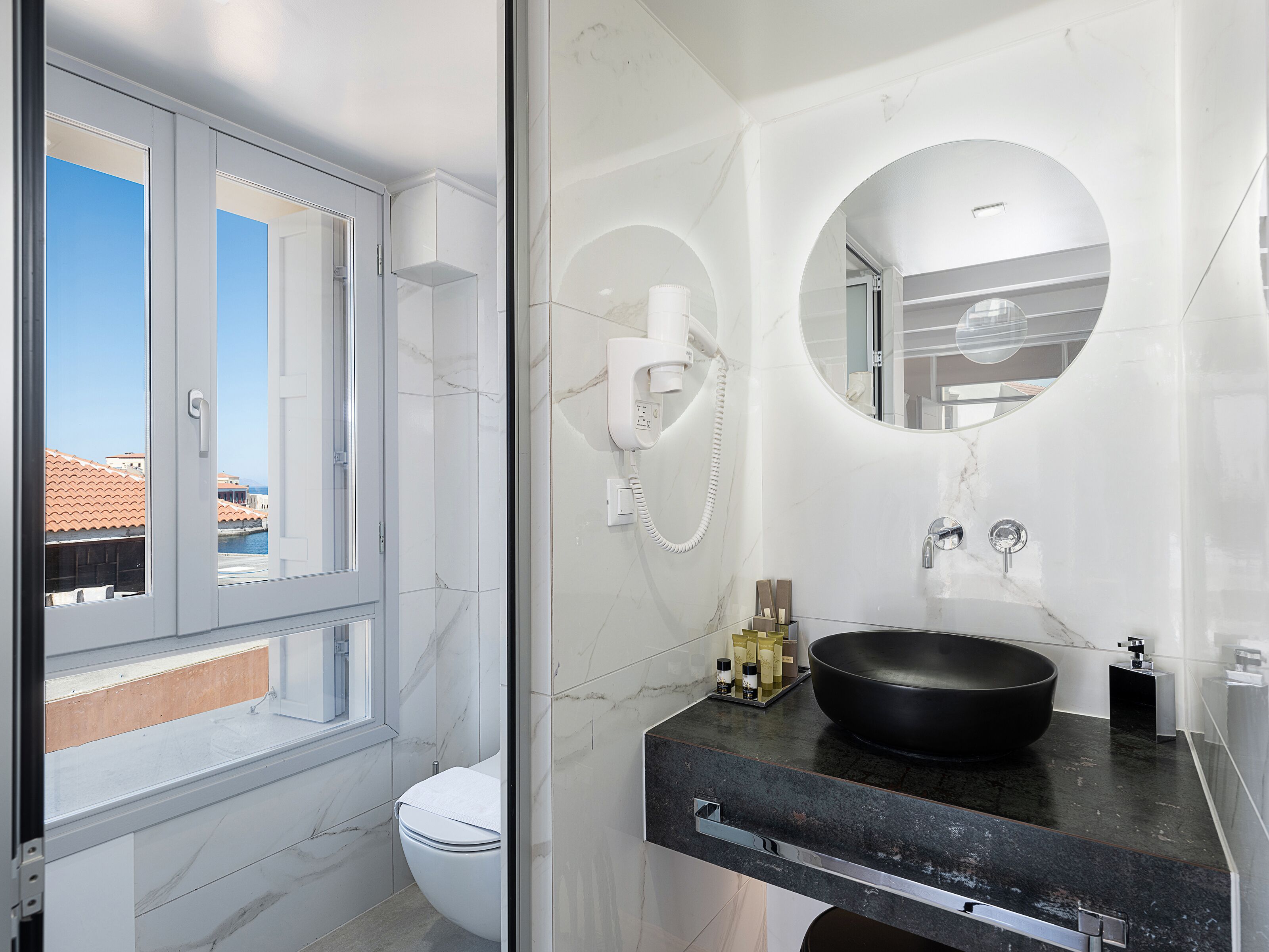 A modern bathroom with a toilet, a large mirror, a black sink, and a shower area.