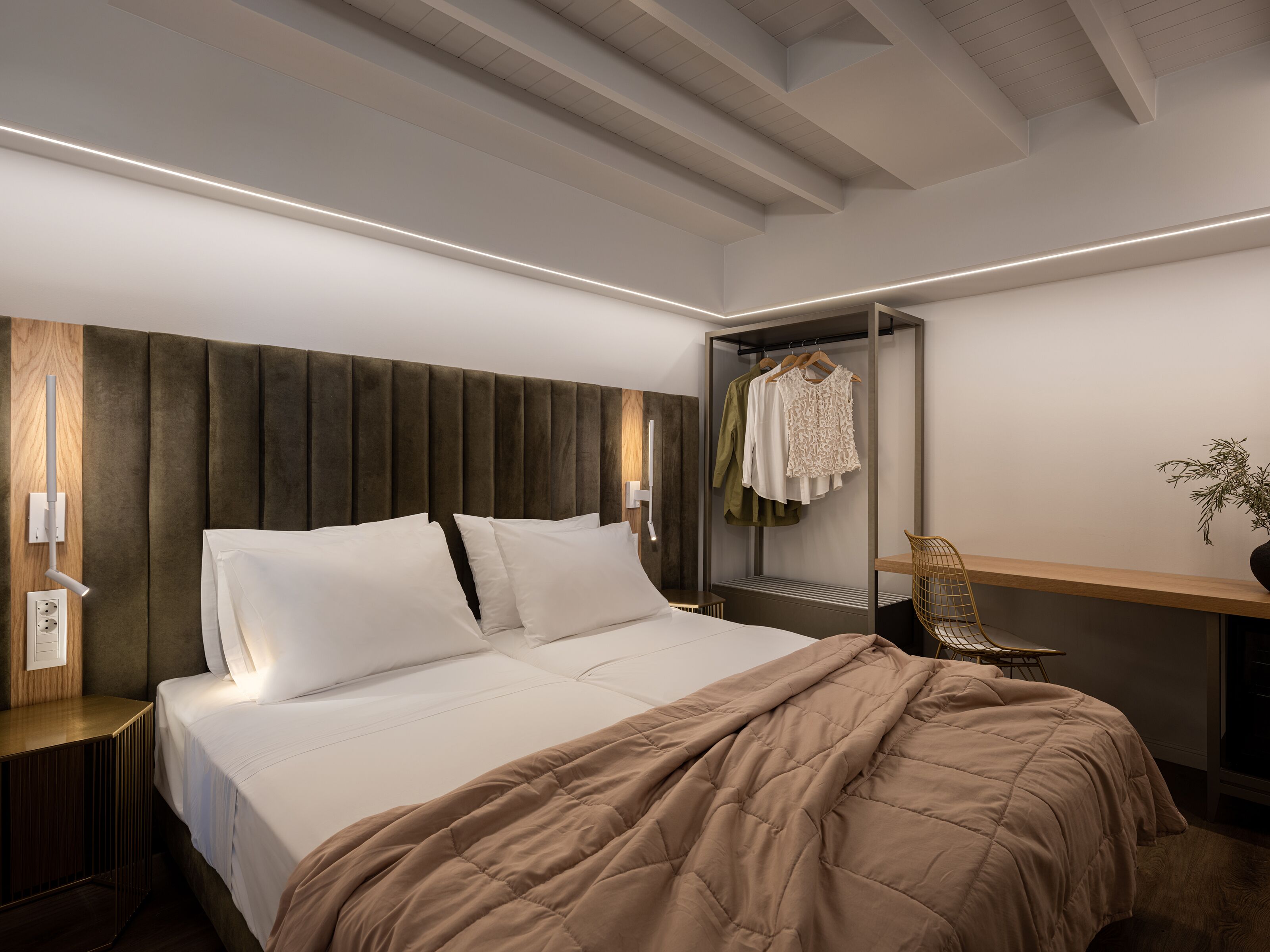 Une chambre moderne avec un grand lit, une tête de lit, des tables de chevet, une armoire et un coin salon comprenant une chaise et une petite table.