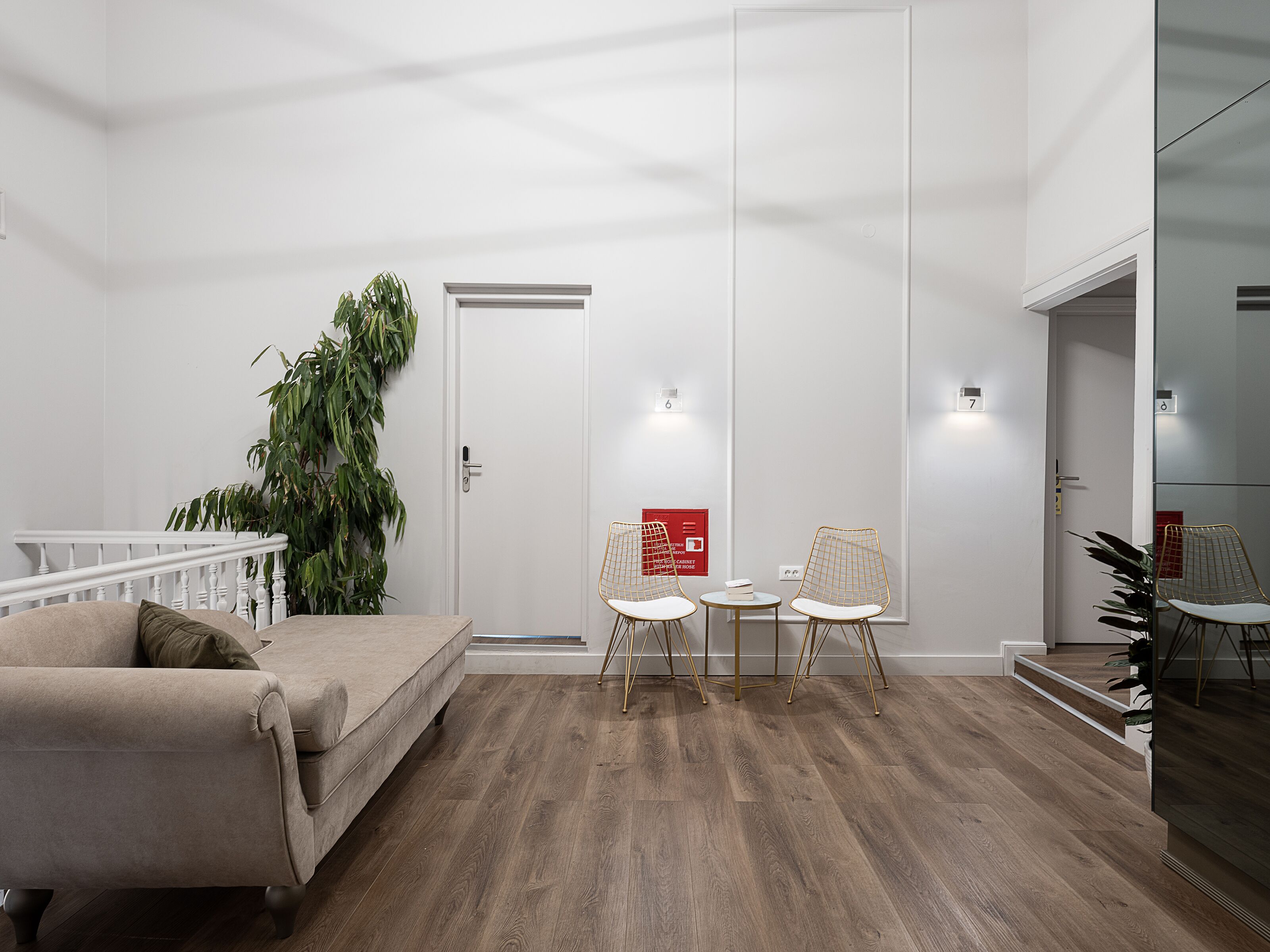 A modern living room with a beige sofa, two white chairs, a small table, and a staircase leading to another level.