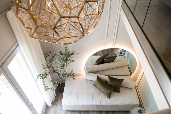 A modern interior with a geometric ceiling light, a potted plant, a cushioned seating area with pillows, and a circular mirror.