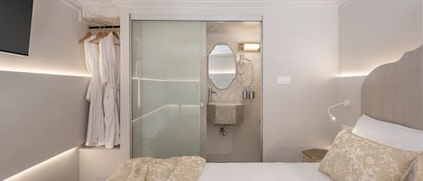 Un dormitorio moderno con una cama grande, un vestidor, un baño con espejo y lavamanos, y un televisor en la pared.