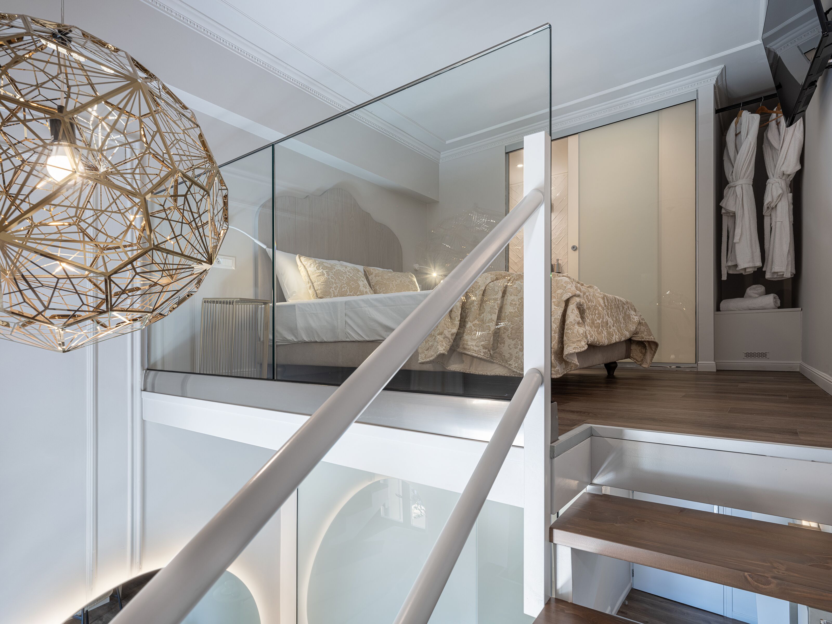 A modern bedroom with a glass staircase, a geometric light fixture, and a bed with a patterned cover.
