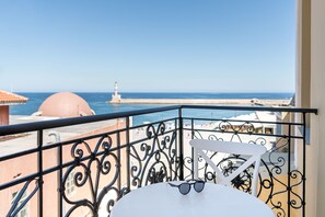 Een balkon met uitzicht op zee, een witte stoel en een paar zonnebrillen op een ronde tafel.