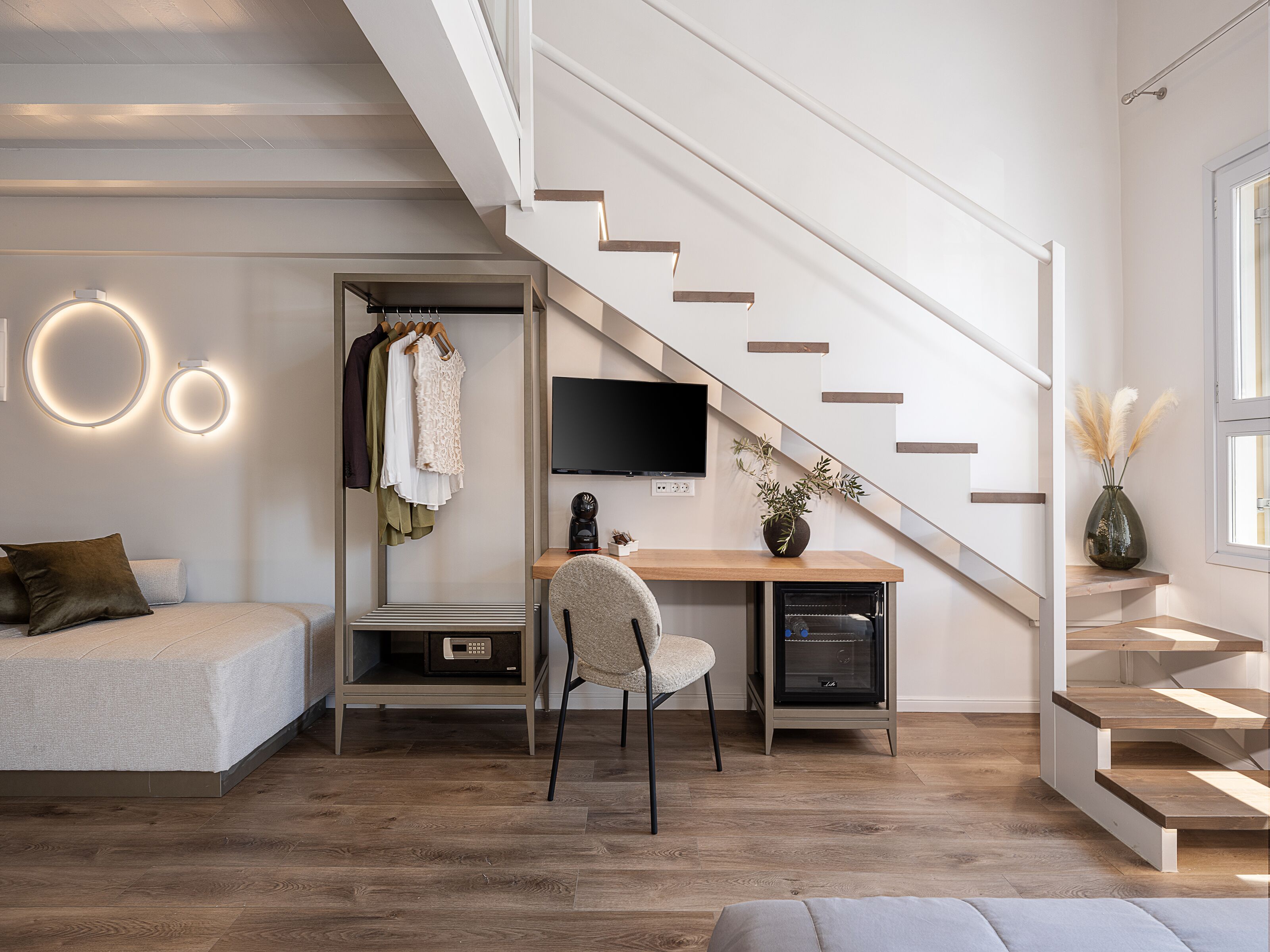 A modern bedroom with a bed, a desk, a chair, a TV, and a staircase.