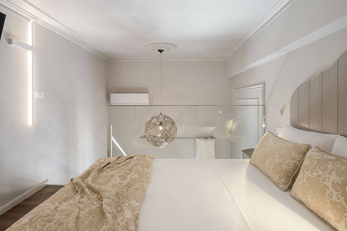 Une chambre avec un grand lit, une cloison en verre et un luminaire au plafond.