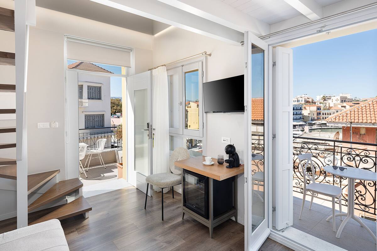Un appartement moderne avec un plancher en bois, un téléviseur fixé au mur et un balcon offrant une vue sur la ville.