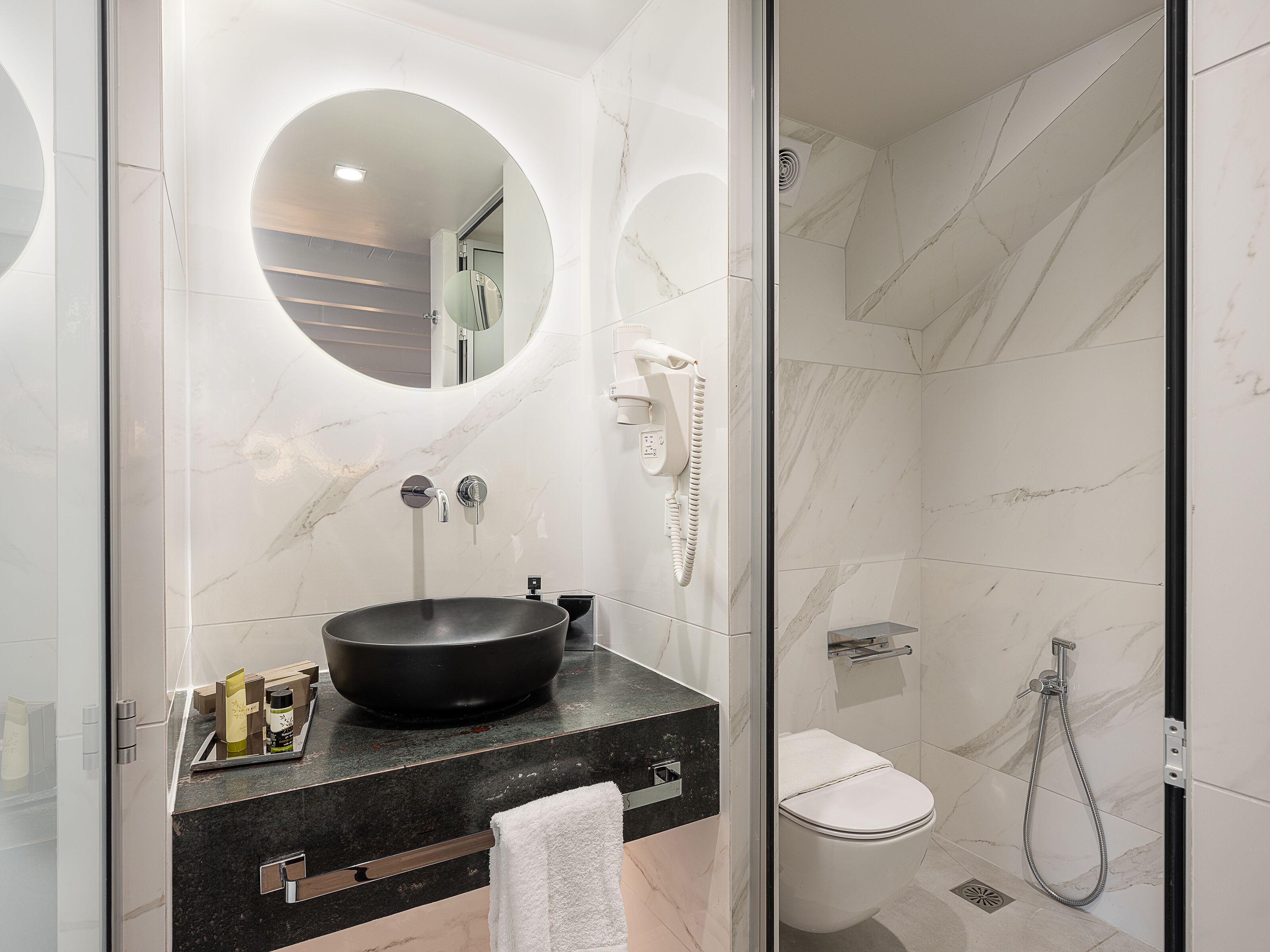 Een moderne badkamer met een ronde spiegel, een zwarte wastafel en een toilet.