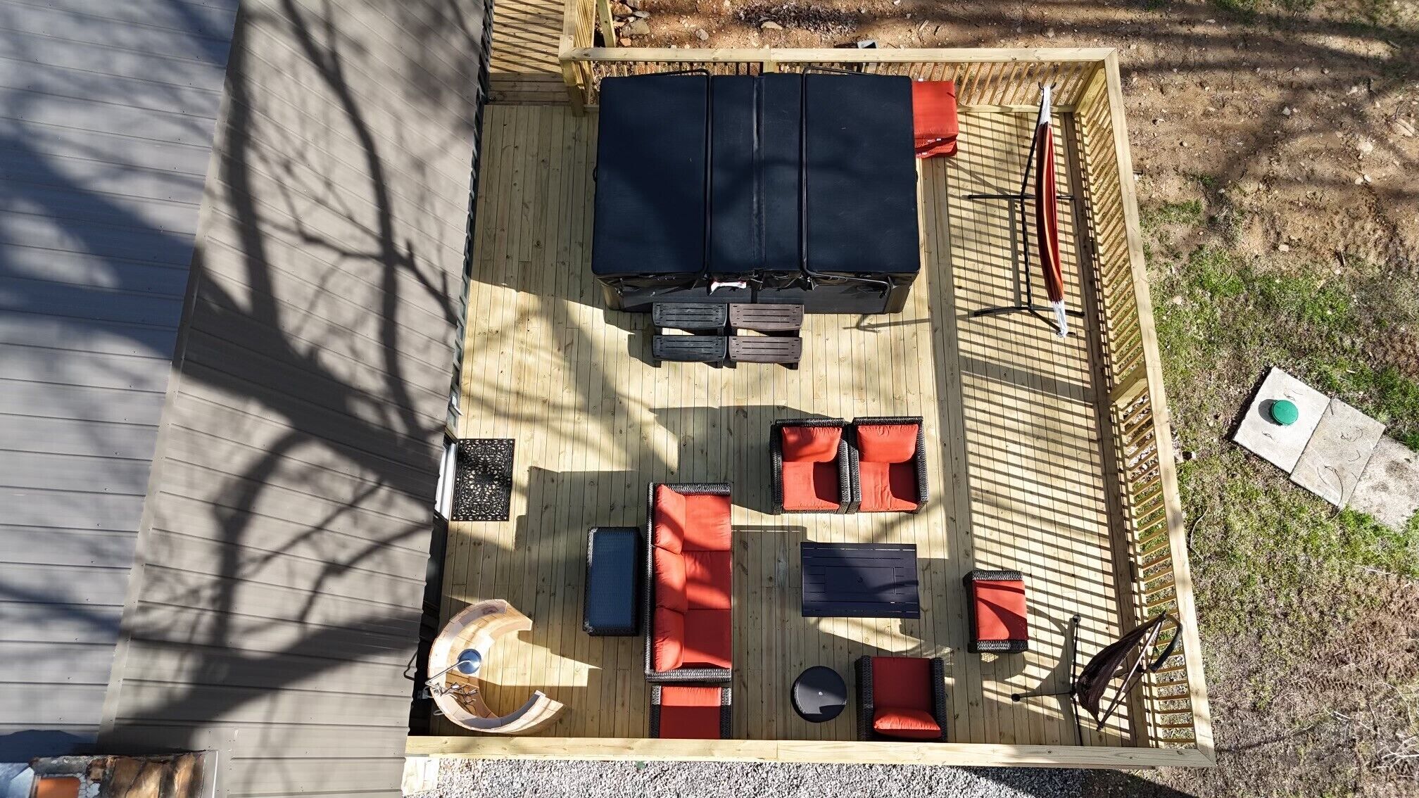 Une terrasse avec un plancher en bois, un espace de détente circulaire agrémenté de coussins, une table rectangulaire et un barbecue.