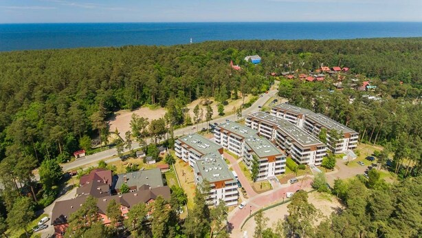 Vista aérea de una zona residencial con varios edificios de apartamentos, rodeada de un bosque denso y una vista despejada del océano.