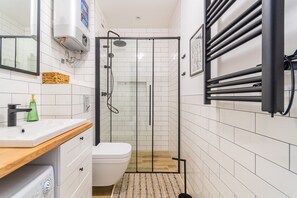 Un baño moderno con ducha de vidrio, inodoro blanco, tocador de madera y perchero para toallas.