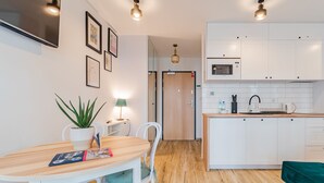 Una cocina moderna con armarios blancos, microondas y encimera de madera. Hay una mesa de comedor con sillas y una planta en maceta.