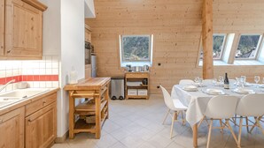 Innenansicht einer Holzhütte mit Küche, Essbereich und großen Fenstern mit Blick auf die Berge.
