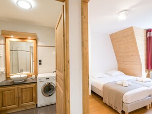 A bedroom with a bed, a wooden headboard, and a bathroom with a sink, mirror, and washing machine.