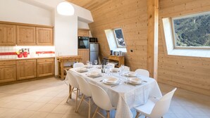 Eine moderne Küche mit Holzschränken, einem Esstisch für sechs Personen und einem großen Fenster mit Blick auf ein bewaldetes Gebiet.
