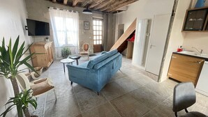 Een woonkamer met een blauwe bank, een televisie, houten kasten, een trap en een potplant.