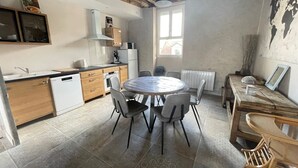 Een kleine keuken met een ronde eettafel en stoelen, een inbouwoven, en een raam dat voor natuurlijk licht zorgt.